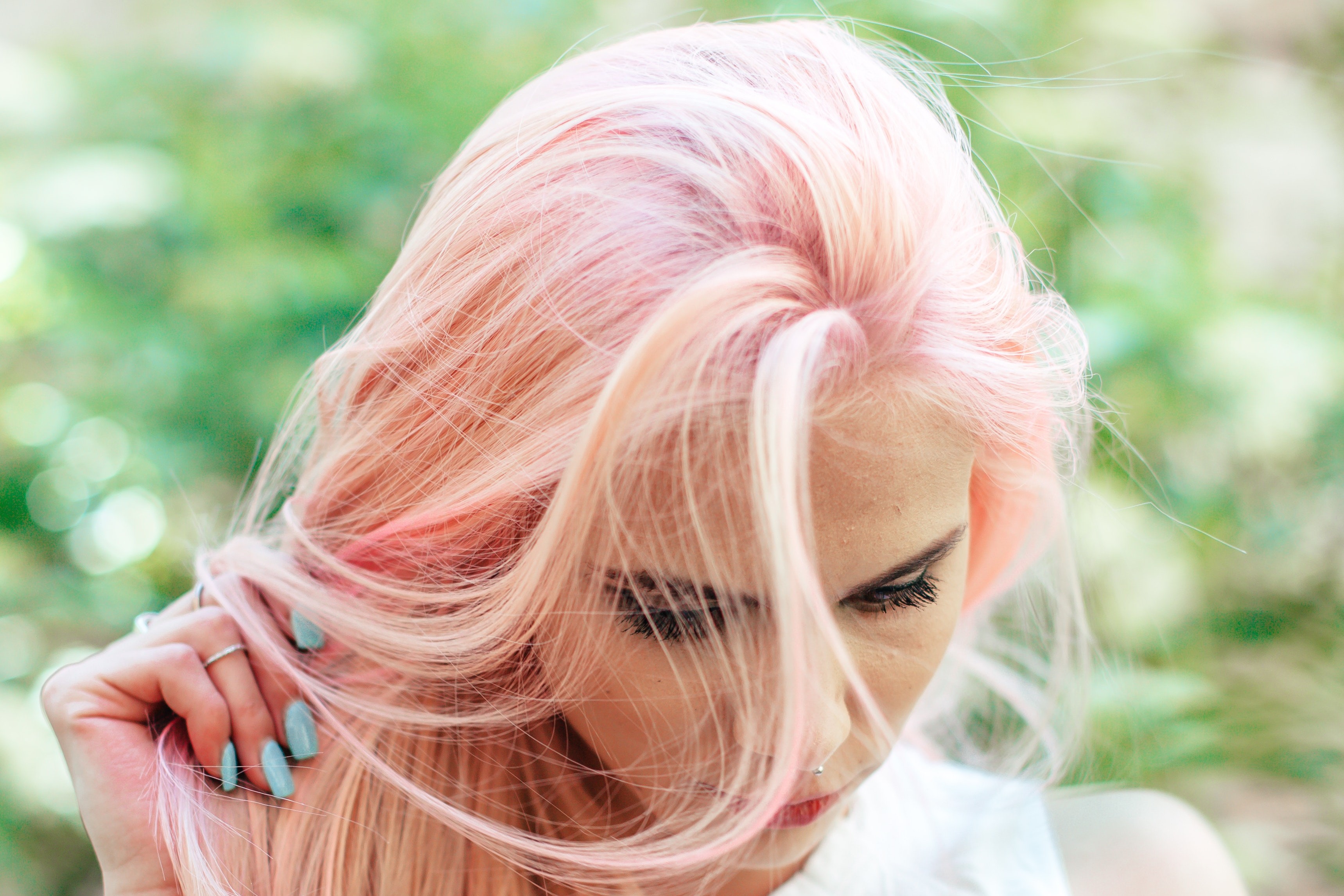 lady with pink hair looks sown whilst holding hair hair in her finger tips