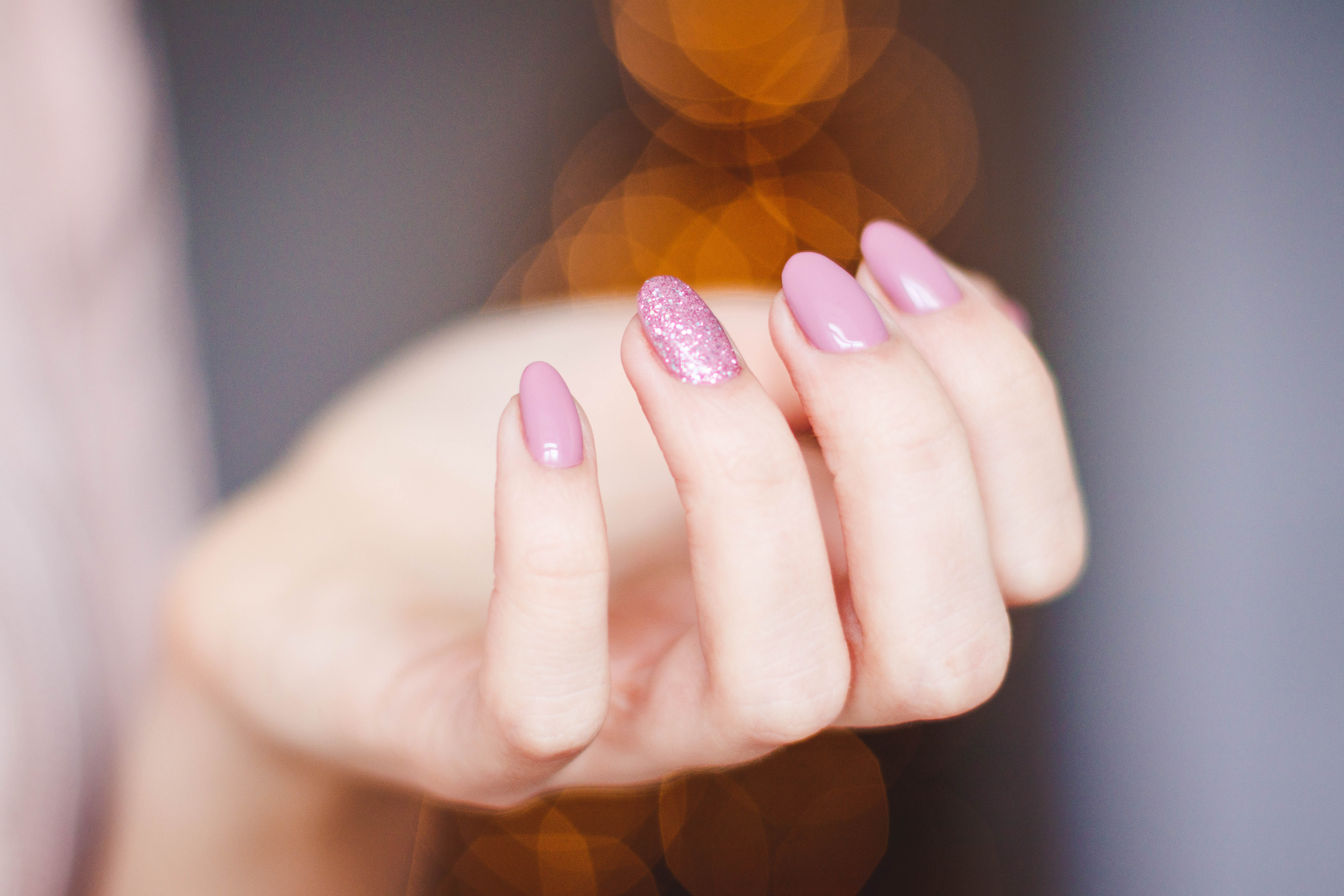 A single hand in focus show pink nails that have been manicured
