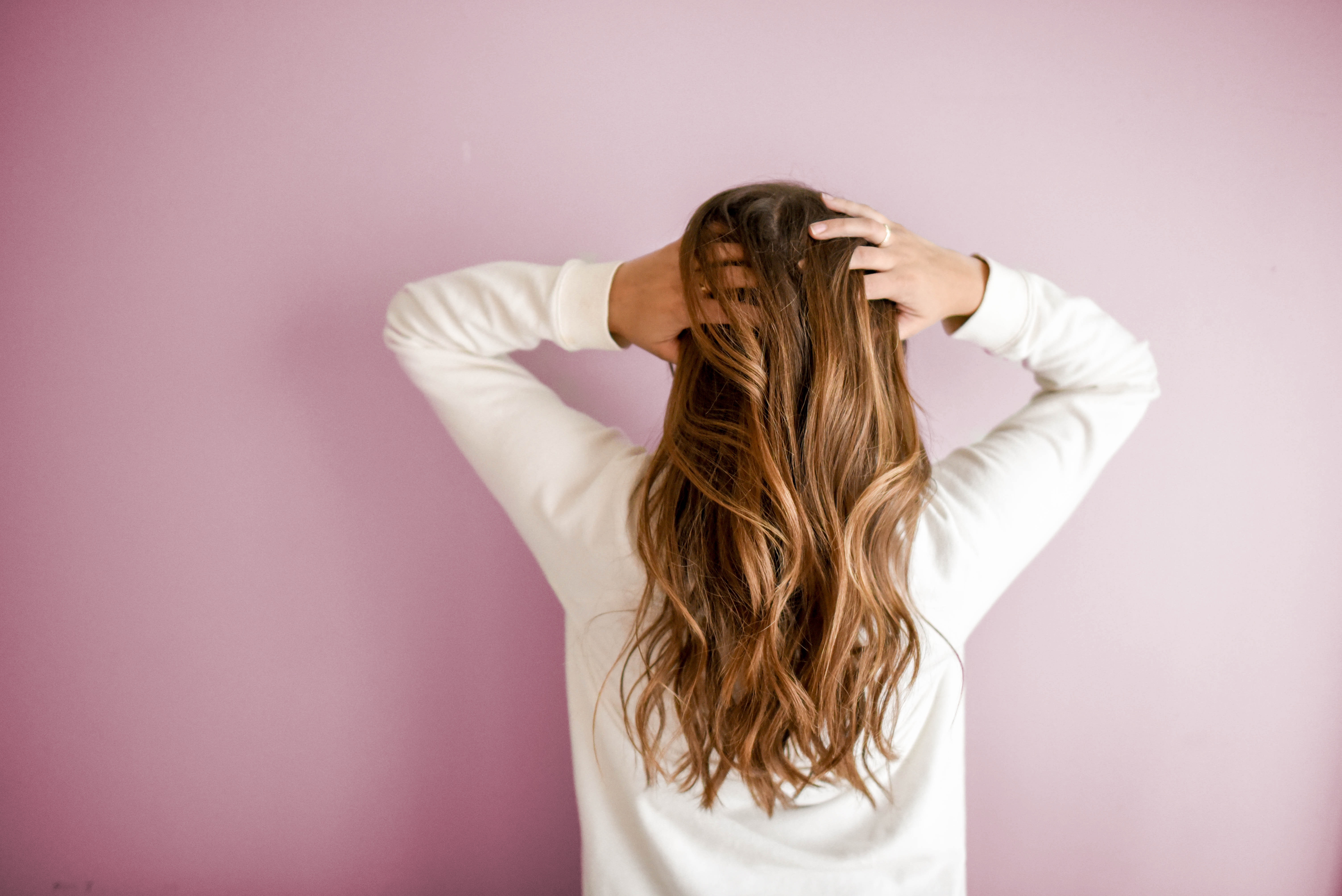 Woman with red hair standing in front of the wall, facing the wall.